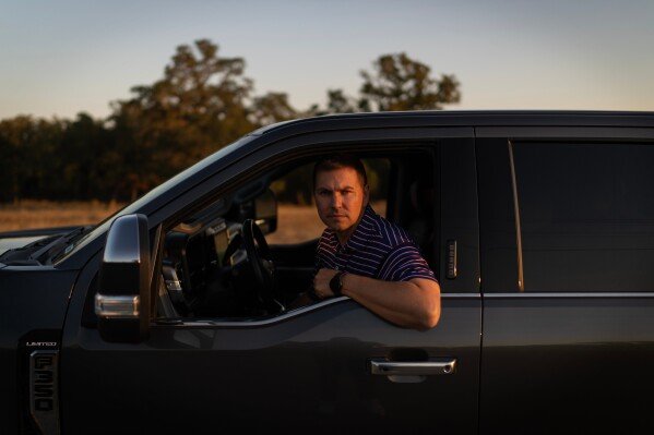 Alek Schott sits for a photo in his car near a route he occasionally takes for work trips Wednesday, Oct. 15, 2025, in Stockdale, Texas. (AP Photo/David Goldman)