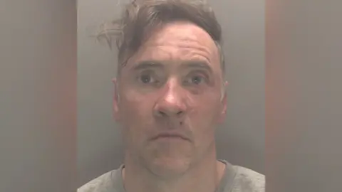 CPS Shot of Paul Doyle wearing a large jacket and looking dazed. His hair has long brown lashes, shaggy and swept to the side. He is wearing a gray shirt.