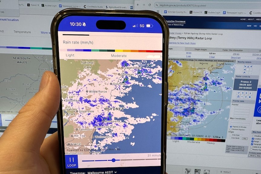 A weather radar being displayed on a phone, in front of a different radar on a computer screen