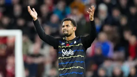 PA Media Iliman Ndiaye wears a black shirt with blue and yellow zigzag stripes. He raised his arms in celebration after scoring a goal.