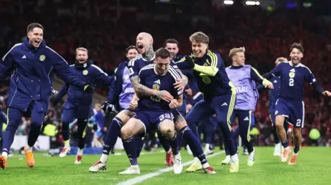 SNS Scotland players in navy blue shirts celebrate with Kenny McLean during Scotland