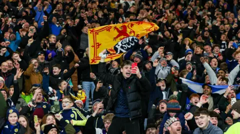 SNS Dozens of Scotland fans celebrate after the final whistle at Hampden. They have scarves and banners.