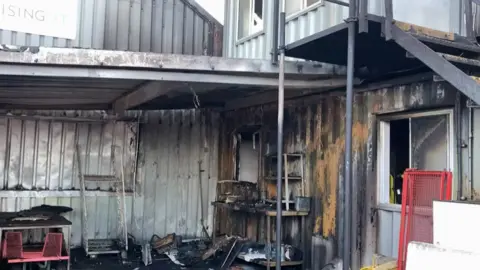 A fire destroyed the portacabin. The metal is burned and there are things on the ground black from smoke. 
