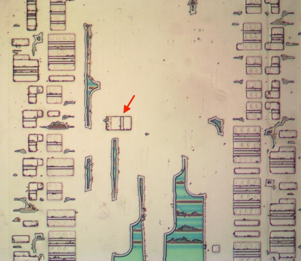 The "misplaced" transistor, indicated by the arrow. The irregular green regions are oxide that was incompletely removed.