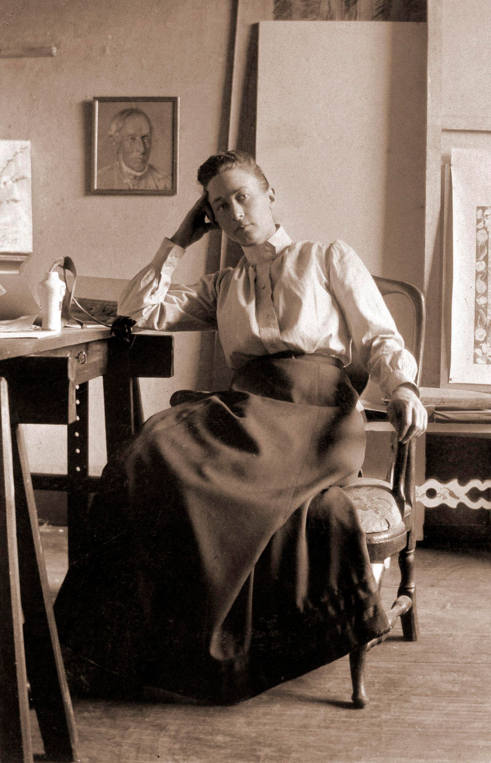 A woman sits on a chair and rests her head on her hand