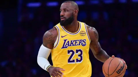 Reuters LeBron James is closeup, dribbling a basketball up the court looking off to his right.. He wears a yellow Los Angeles Lakers Jersey, with number 23 on the front. He has a white arm band on his right arm.