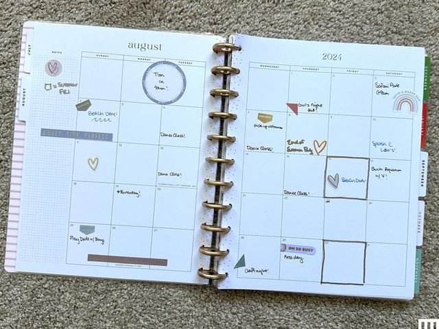 A paper chart is open and laid flat on the carpet, and the pages show notes and labels on top of the grid for the days of August