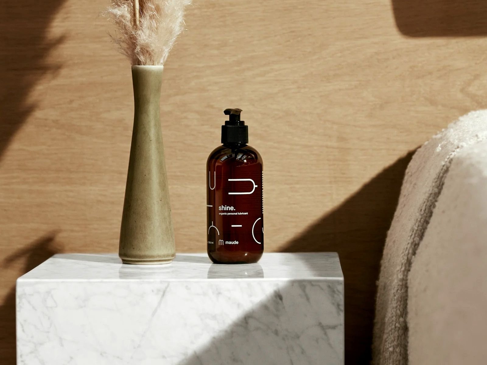 A bottle of Maude Shine Lube is on the bedside table
