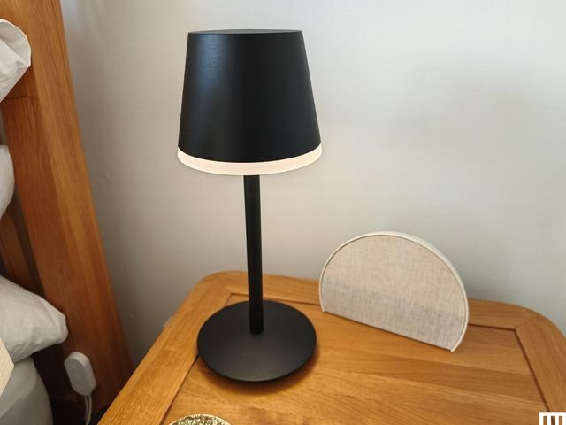 Black lamp beside a semi-circle clock, both sitting on a wooden bedside table