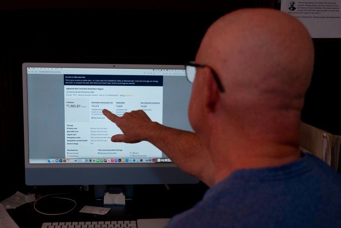 Mike Plante points at health insurance plan details on a computer screen, highlighting yearly cost and deductible amounts.