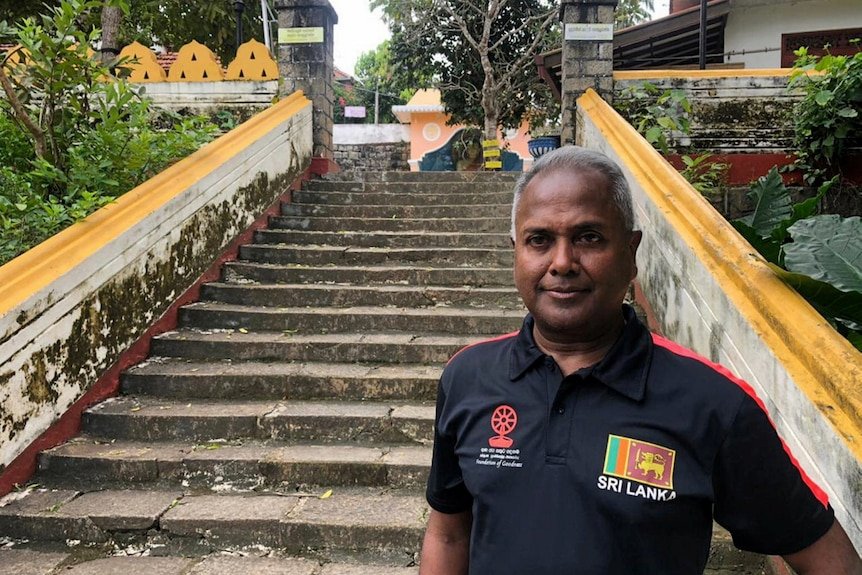 A man poses for a portrait at the bottom of a set of steps outside.