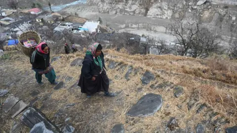 Getty Images In this picture taken on February 10, 2021, women from Raini Chak Lata village walk along a mountain path in Chamoli district. - Long before this month