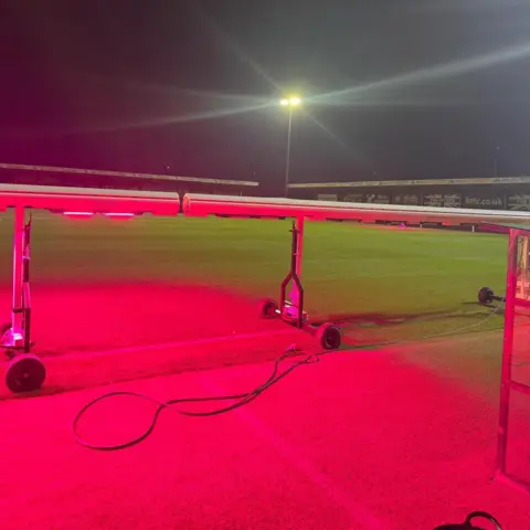Hednesford Town Football Club Hednesford Town Football Club is equipped with pink LED lights used to treat the corner of the pitch. A spotlight can be seen in the background, illuminating the grass.  
