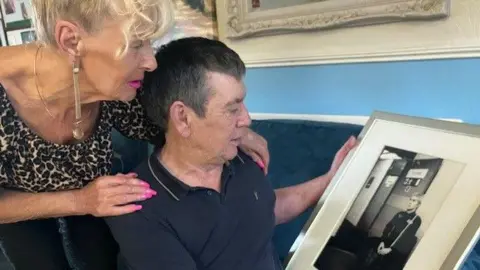 David Sperrill/BBC Christina and Alan Hunter observe a framed monochrome photograph of Paul Hunter. Alan sat down. Cristina stands behind him and puts her arms around his shoulders.