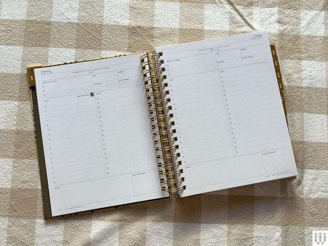 Top view of Day Designer Daily Planner open on beige and white checkered cloth, interior pages showing blank to-do lists