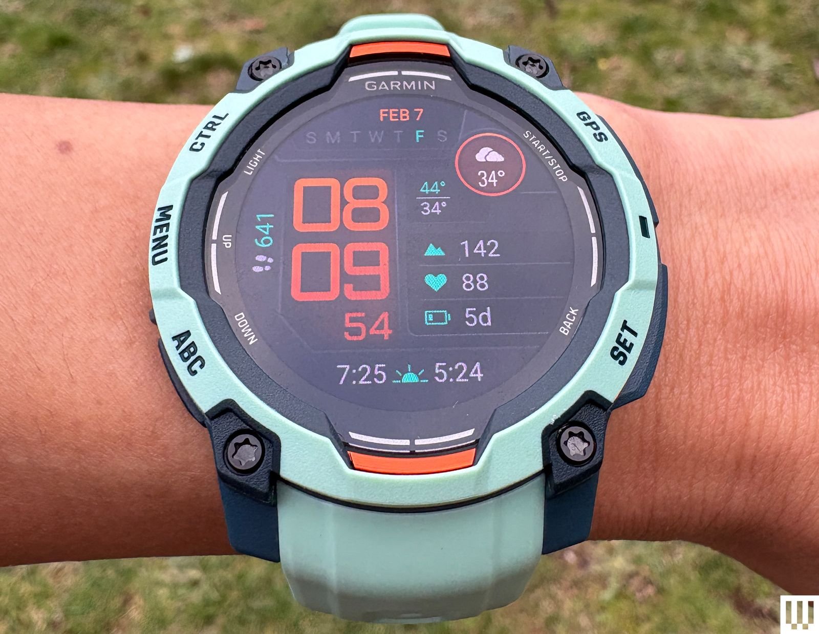 Top view of a wrist wearing Garmin Instinct 3, a teal fitness tracker with a large digital display