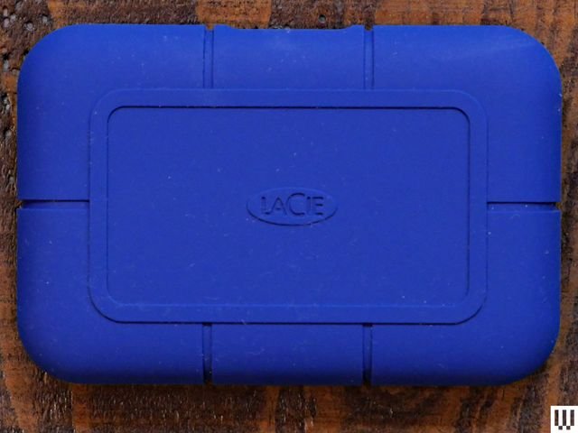 Overhead view of a LaCie Rugged SSD Pro5 external hard drive, a blue rounded rectangular device on a wooden surface