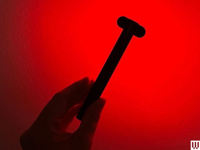 A hand holds the Solawave Radiant Renewal Want, a slim black device with red lights burning from the oval top.