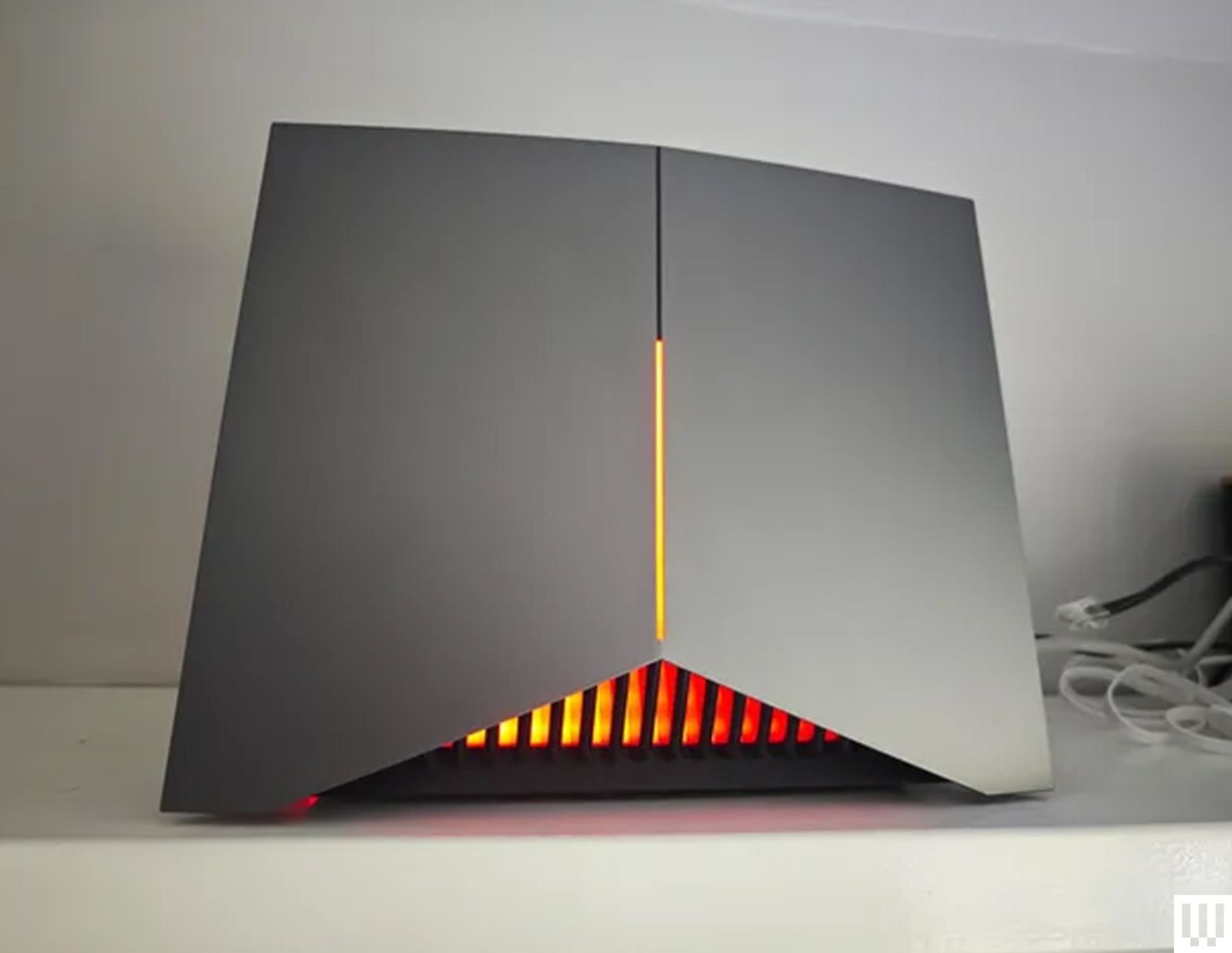 The TP Link Archer GE800 wifi router sitting on a shelf a black device with angular bottom and orange illuminated panels