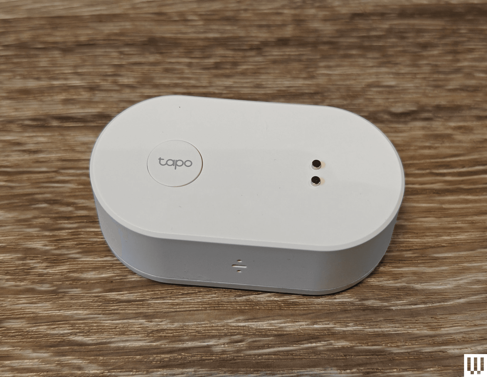 A white, oval-shaped device placed on a wooden surface. The product is branded as Tapo.