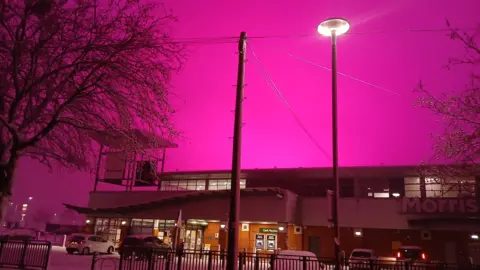 GLMCC Pink skies above Morrisons supermarket in the Small Heath area of ​​Birmingham. The supermarket is illuminated by the snow visible in its parking lot and bright street lighting. 