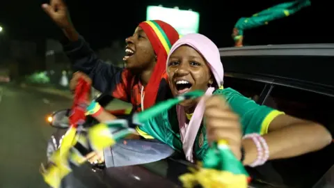 Reuters Two Senegalese fans wearing national colors cheer as they get out of a moving car.