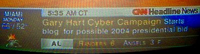 A photo from 2004 of a TV screen showing CNN, with a ticker saying "Gary Hart Cyber Campaign Starts blog for possible 2004 presidential bid"