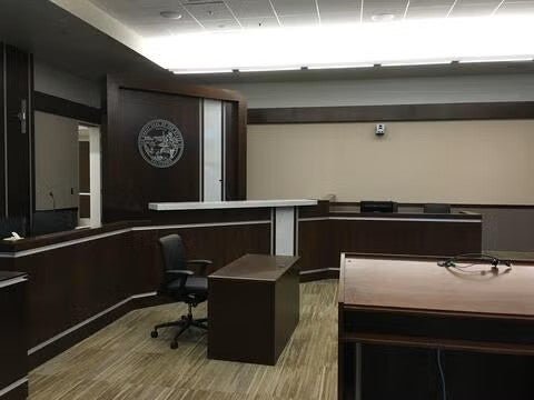 Courtroom with dark brown podium in the foreground. Dark brown desks line the room and the judicial seal is on the wall.