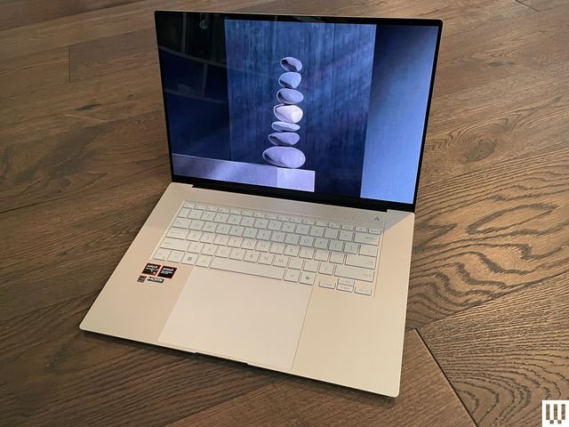 Asus Zenbook S 16, front view of a silver laptop sitting on a hardwood floor.