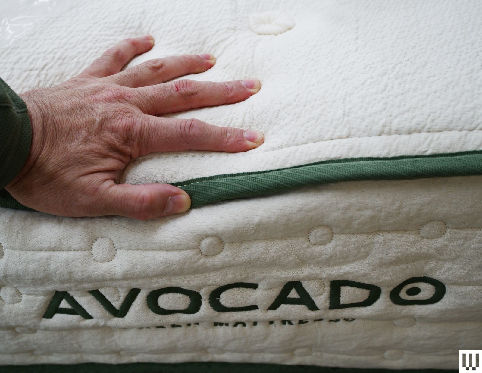 Close-up of a hand pushing down on an avocado green mattress showing the thick white side with green trim