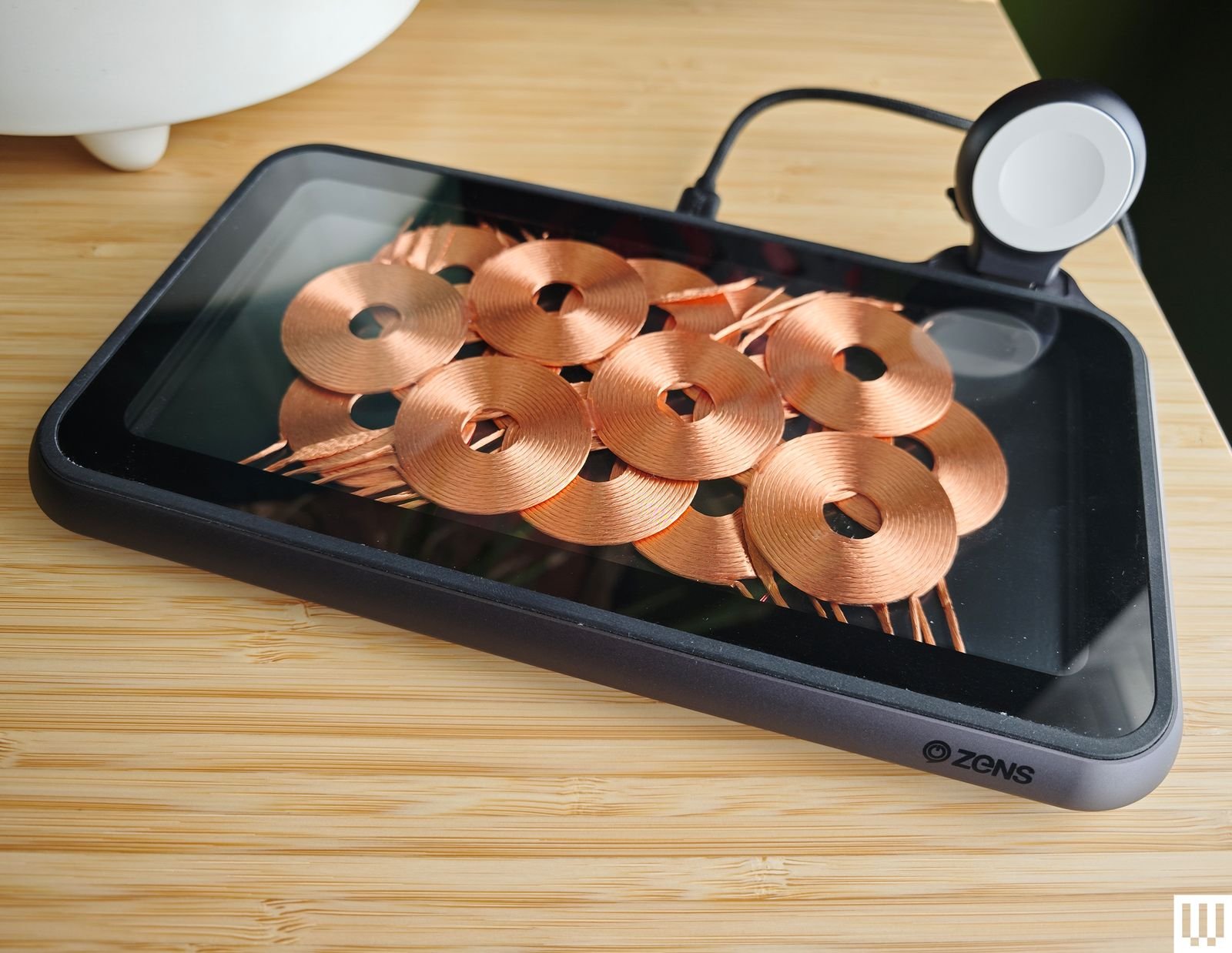 Zens Liberty Wireless Charger Glass Edition is a mobile phone that sits on a small charging pad on the edge of a table