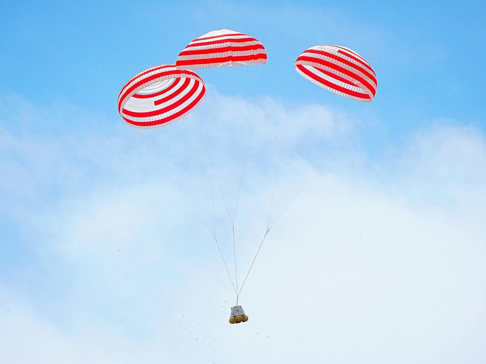A manned spacecraft with deployed parachutes gently descending back to Earth.