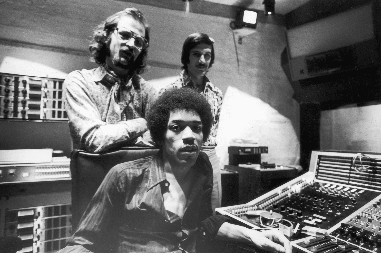 A photograph of three young men beside a recording studio mixing desk.