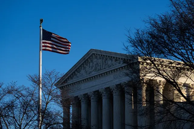 View of the columns at the US Supreme Court. A US flag on a pole is in the foreground on the left.