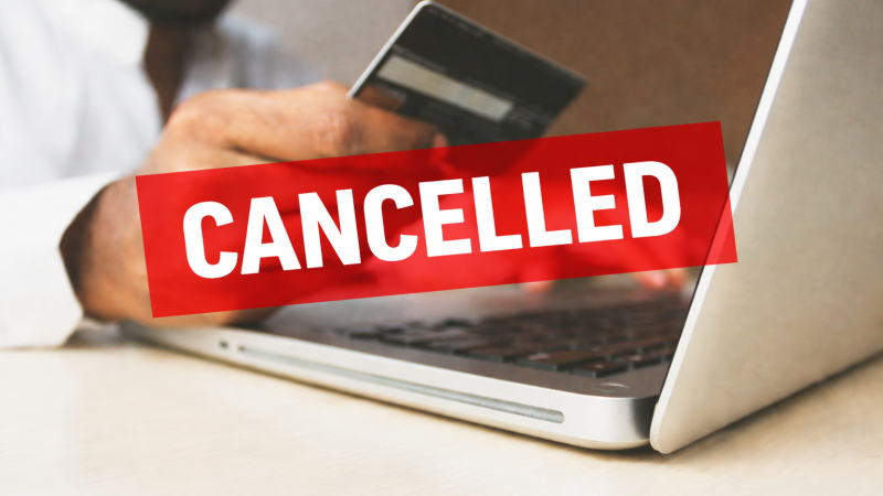 A person holds a credit card while using a laptop for an online transaction. A bold red banner with the word “cancelled” is overlaid across the image, indicating the payment or card has been blocked.